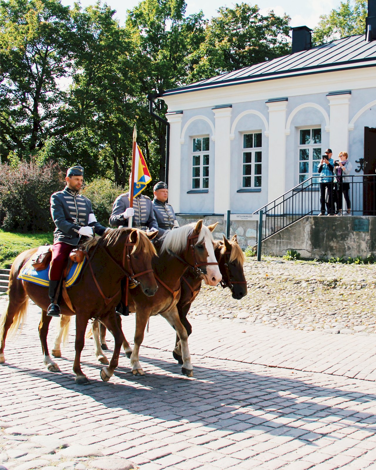 Kolme univormuihin pukeutunutta miestä ratsastavat hevosilla Lappeenrannan linnoituksen pihapiirissä.